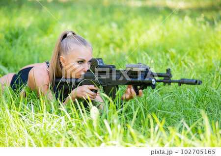 Caucasian woman in bikini lies with machine gun on green grass. Caucasian woman in bikini lies with machine gun on green grass. 102705165