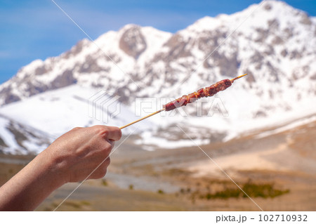 hand hold Arrosticino - typical Abruzzese sheep skewer - grilled with mountains of Gran Sasso hand hold Arrosticino - typical Abruzzese sheep skewer - grilled with mountains of Gran Sasso 102710932
