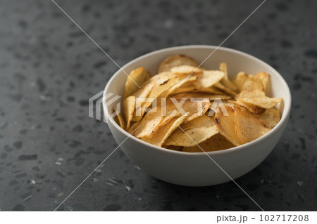 Organic potato chips with black pepper in white ceramic bowl on concrete background with copy space Organic potato chips with black pepper in white ceramic bowl on concrete background with copy space 102717208