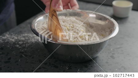 man mixing wet ingredients into flour in steel bowl on concrete countertop 102717443