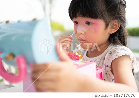 Adorable little child Asian girl paints her mouth with pink children heads and looks in the mirror. A child plays at home in a toy beauty salon. Increase learning development for preschoolers. Adorable little child Asian girl paints her mouth with pink children heads and looks in the mirror. A child plays at home in a toy beauty salon. Increase learning development for preschoolers. 102717676