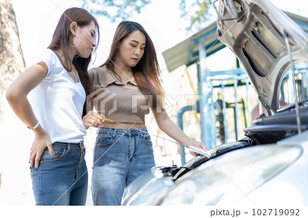 Two Asian people try to check the car engine and wait for assistance after a car breakdown on street. Concept of a vehicle engine problem or accident and emergency help from a Professional mechanic 102719092