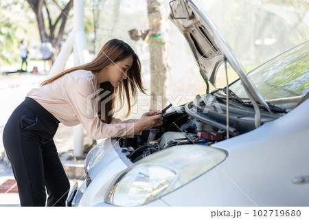 Angry Asian woman using a smartphone VIDEO conference for assistance after a car breakdown on street. Concept of a vehicle engine problem or accident and emergency help from a Professional mechanic 102719680