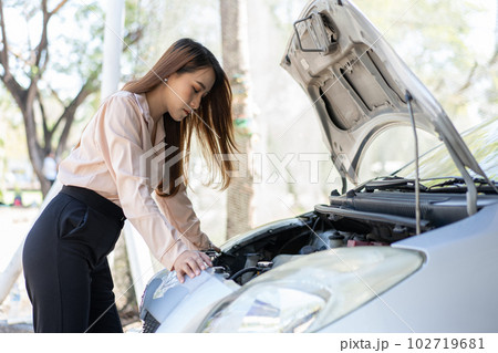 Angry Asian woman using a smartphone VIDEO conference for assistance after a car breakdown on street. Concept of a vehicle engine problem or accident and emergency help from a Professional mechanic 102719681