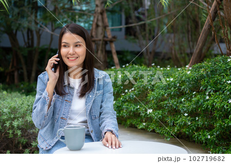Young Asian woman freelancer holding smartphone for talking with friend. Lifestyle women working at home concept. sitting in thicket of tropical. Girl on holiday sitting in garden smiling relaxing. Young Asian woman freelancer holding smartphone for talking with friend. Lifestyle women working at home concept. sitting in thicket of tropical. Girl on holiday sitting in garden smiling relaxing. 102719682