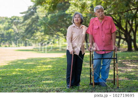 An old elderly Asian man uses a walker and walks in the park with his wife. Concept of happy retirement With Love and care from family and caregiver, Savings, and senior health insurance An old elderly Asian man uses a walker and walks in the park with his wife. Concept of happy retirement With Love and care from family and caregiver, Savings, and senior health insurance 102719695