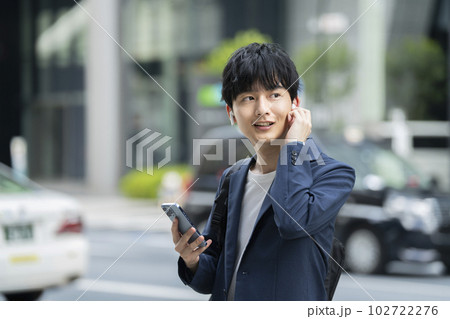 スマートフォンを持ちワイヤレスイヤホンをつけた若い男性 スマートフォンを持ちワイヤレスイヤホンをつけた若い男性 102722276