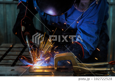 Worker in heavy industry, wearinga protective mask and welds steel other metals an industrial setting Worker in heavy industry, wearinga protective mask and welds steel other metals an industrial setting 102722528
