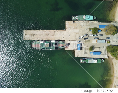 Ferry boat crossing the sea, carrying cars and passengers. Cars drive off the deck onto the port. Top-down aerial drone view Ferry on the lake, transporting cars: deck of a boat carrying vehicles. Ferry boat crossing the sea, carrying cars and passengers. Cars drive off the deck onto the port. Top-down aerial drone view Ferry on the lake, transporting cars: deck of a boat carrying vehicles. 102723921