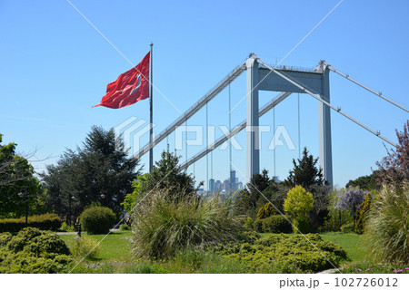 The Turkish flag is waving in the wind in a park overlooking the bridge over the Bosphorus and beautifully blooming sakura. Travel Istanbul background photo. 102726012