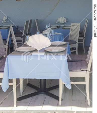 Beautiful table setting with glasses, tablecloth, plates in a nautical style in a fish restaurant, blue tinted Beautiful table setting with glasses, tablecloth, plates in a nautical style in a fish restaurant, blue tinted 102729796
