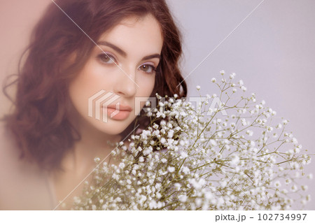 A brunette girl holds a bouquet of gypsophila flowers in her hands. A brunette girl holds a bouquet of gypsophila flowers in her hands. 102734997