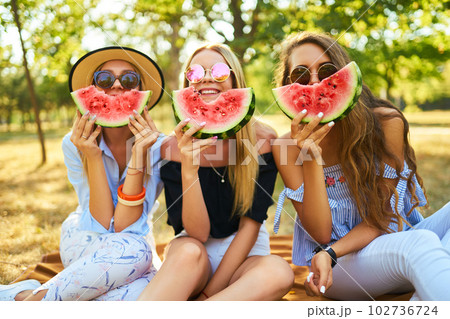 Three nice girls having fun eating watermelon In the park. Excellent sunny weather. Beautiful figures 102736724