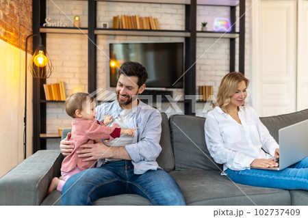 Father carrying infant daughter mother using laptop remote work husband helping with baby child 102737409