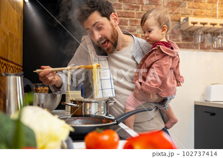 Father looking after baby girl making meal and talking on mobile phone, multitasking man. 102737414