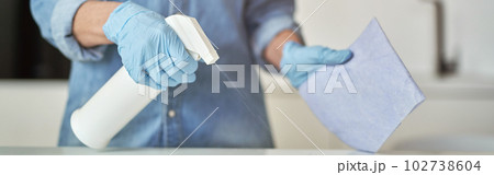 Close up shot of female hands in rubber gloves using detergent spray and cloth while cleaning kitchen surface Close up shot of female hands in rubber gloves using detergent spray and cloth while cleaning kitchen surface 102738604