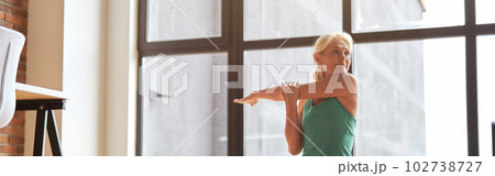 Charming mature blonde woman looking aside, sitting on the floor while practicing yoga with laptop at home in the daytime Charming mature blonde woman looking aside, sitting on the floor while practicing yoga with laptop at home in the daytime 102738727