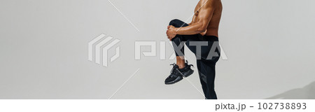 Athletic man with naked torso doing leg stretching exercises before workout on studio background Athletic man with naked torso doing leg stretching exercises before workout on studio background 102738893