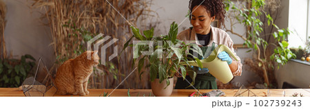 Smiling woman florist taking care of plant watering it in floral shop Smiling woman florist taking care of plant watering it in floral shop 102739243