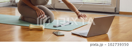 Afro american sporty woman sit on floor and preparing for online fitness class from home Afro american sporty woman sit on floor and preparing for online fitness class from home 102739350
