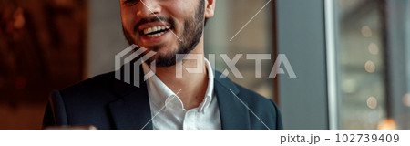 Smiling Indian businessman wearing suit is using phone during lunch time in cafe 102739409