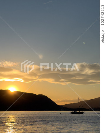 Sailing yacht floats on the sea against the backdrop of sunset over the mountains Sailing yacht floats on the sea against the backdrop of sunset over the mountains 102742215