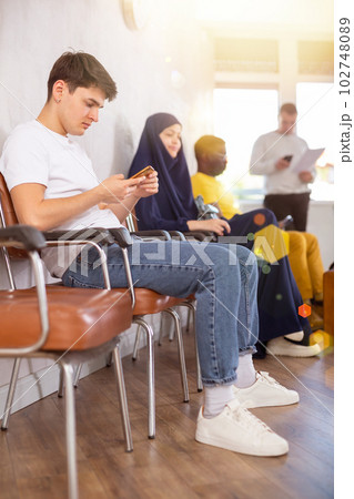 Young man communicates on mobile phone while sitting on chair in the company office waiting for specialist 102748089