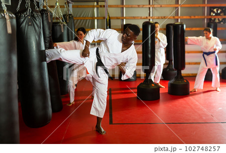 African american man in kimono practicing powerful body punches on heavy punchbag African american man in kimono practicing powerful body punches on heavy punchbag 102748257
