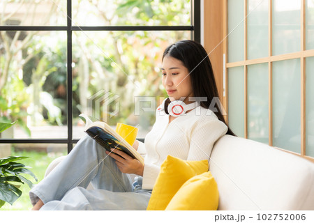 Happy young woman reading book on sofa at home.  Lifestyle freelance 102752006