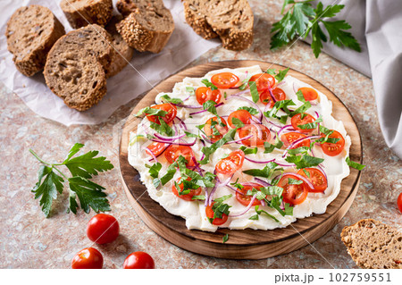 Trendy butter board with tomatoes, onions and parsley and slices of bread on the table Trendy butter board with tomatoes, onions and parsley and slices of bread on the table 102759551