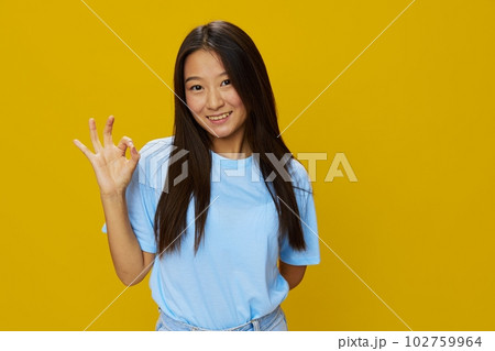 Asian woman smile with teeth hand gestures, signs and symbols on yellow background in blue t-shirt and jeans Asian woman smile with teeth hand gestures, signs and symbols on yellow background in blue t-shirt and jeans 102759964
