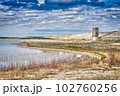 The grandiose architecture of San Angelo State Park in Texas rises out of the lush marshlands, its history visible against a shimmering lake and horizon full of fluffy clouds. 102760256