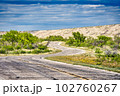 A tranquil landscape of a cloud-filled sky over an expansive dam, tree-lined roads and plants in San Angelo State Park, Texas. 102760267