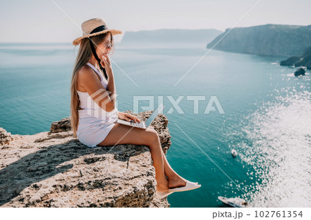 Digital nomad, Business woman working on laptop by the sea. Pretty lady typing on computer by the sea at sunset, makes a business transaction online from a distance. Freelance, remote work on vacation 102761354
