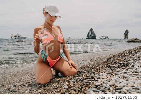 Woman travel sea. Happy tourist in pink bikini enjoy taking picture outdoors for memories. Woman traveler posing on the beach at sea surrounded by volcanic mountains, sharing travel adventure journey 102761569