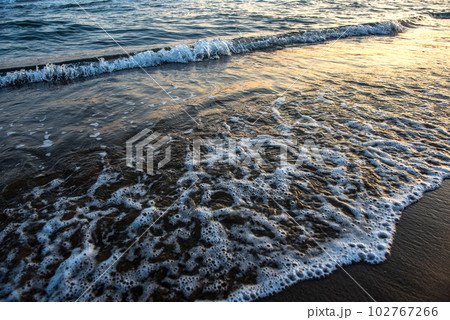 Waves approaching sandy beach during sunset 102767266