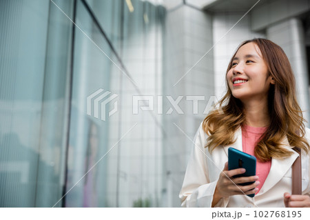 Asian businesswoman texting smartphone commuting work she walking near her office building in morning, Beautiful business woman smiling hold mobile phone outdoor walking on city street urban Asian businesswoman texting smartphone commuting work she walking near her office building in morning, Beautiful business woman smiling hold mobile phone outdoor walking on city street urban 102768195