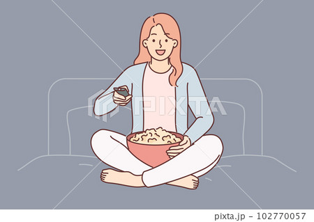Woman with TV remote turns on series sitting on bed in bedroom and holds cup of popcorn 102770057