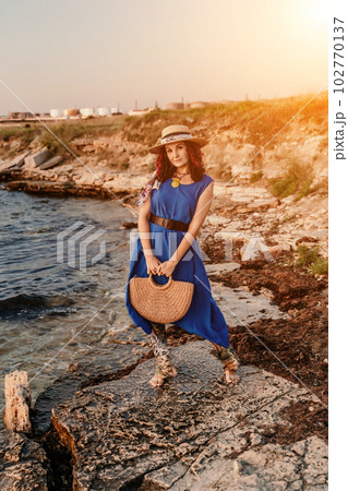 A woman in a dress, hat and with a straw bag is standing on the 102770137