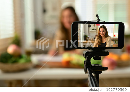 Confident female blogger holding celery, providing with online consultations or recording video content on smartphone 102770560