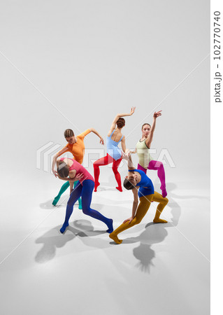 Group of talented, artistic female ballet dancers in bright, multicolored clothes performing against grey studio background 102770740