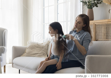 Caring young mom brushing black long hair of girl kid 102771008