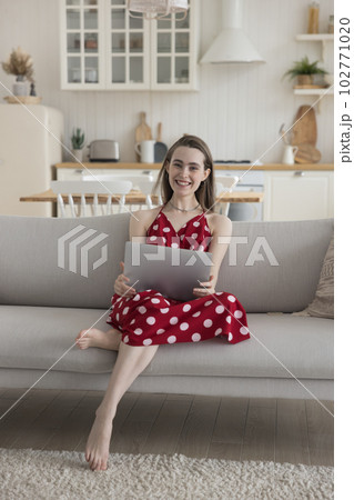 Cheerful pretty young adult girl using laptop on sofa 102771020