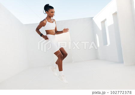Full length of a slim female in white sportswear jumping outdoors. Professional fitness athlete doing warming up exercises. 102772378