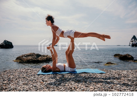 Woman sea yoga. Two Happy women meditating in yoga pose on the beach, ocean and rock mountains. Motivation and inspirational fit and exercising. Healthy lifestyle outdoors in nature, fitness concept. Woman sea yoga. Two Happy women meditating in yoga pose on the beach, ocean and rock mountains. Motivation and inspirational fit and exercising. Healthy lifestyle outdoors in nature, fitness concept. 102772418