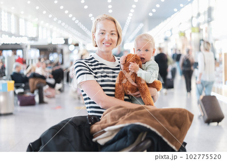 Mother traveling with child, holding his infant baby boy at airport terminal waiting to board a plane. Travel with kids concept 102775520