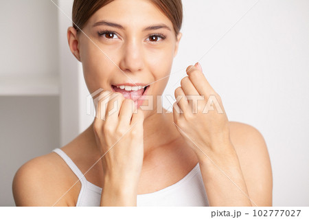 Woman using dental floss for cleaning her teeth Woman using dental floss for cleaning her teeth 102777027