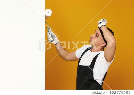 young man in working clothes painting white walls 102779503