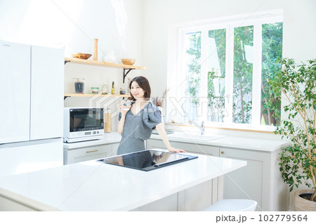 キッチンでコップを持つ若い女性 102779564