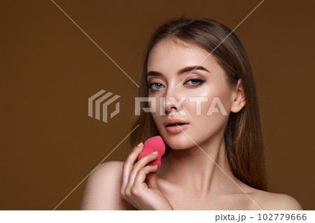 woman applying foundation on skin with beauty blender on beige background 102779666